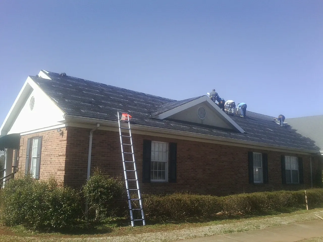 Crew tearing shingles off a brick ranch roof with a ladder set — Emergency Roof Repair work by our crew in Parish