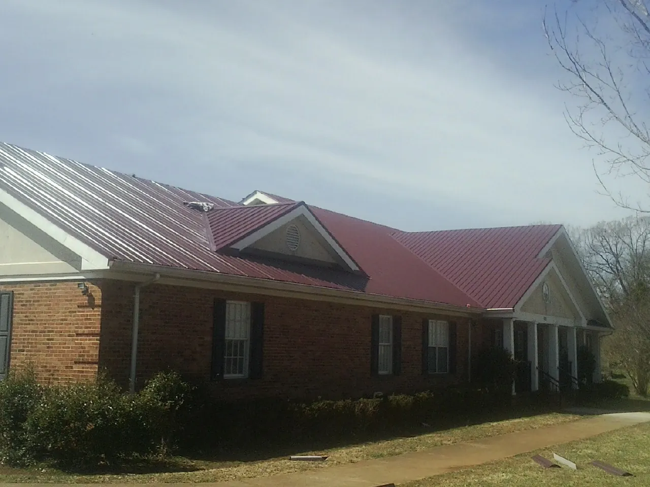 Red metal roof with gabled entries on a long brick building, from a Hail Damage Roof Repair job in Parish