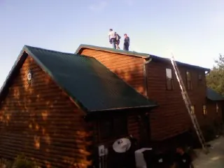 Crew on the ridge of a green metal roof on a two story log home in Parish