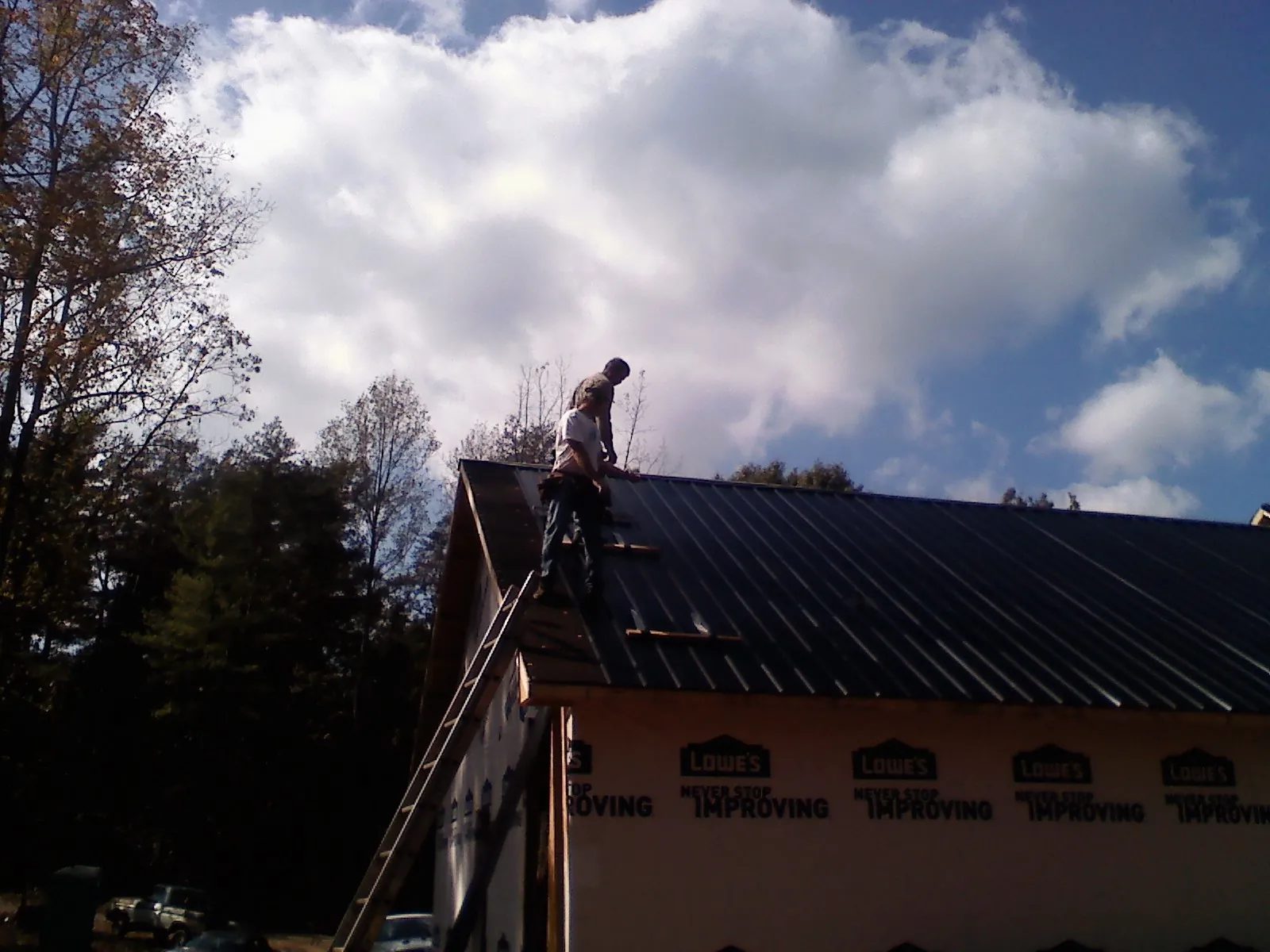 Roofer fastening dark metal panels high against a cloudy sky, from a Roof Inspection job in Parish