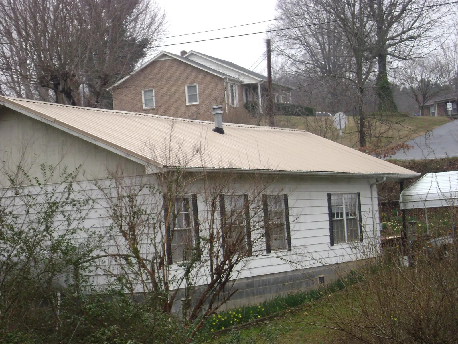 Tan metal roof on a white sided house set into a hillside — Commercial Roofing by Roofing Brothers in Parish