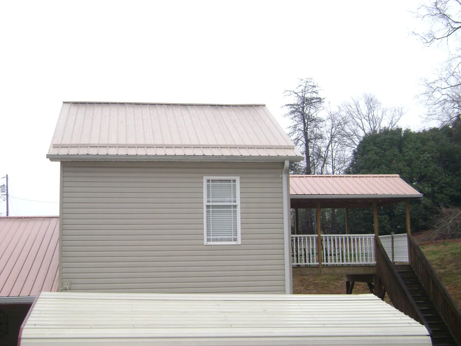 Tan metal roofs on a two story addition and attached porch, from a Roof Replacement job in Parish